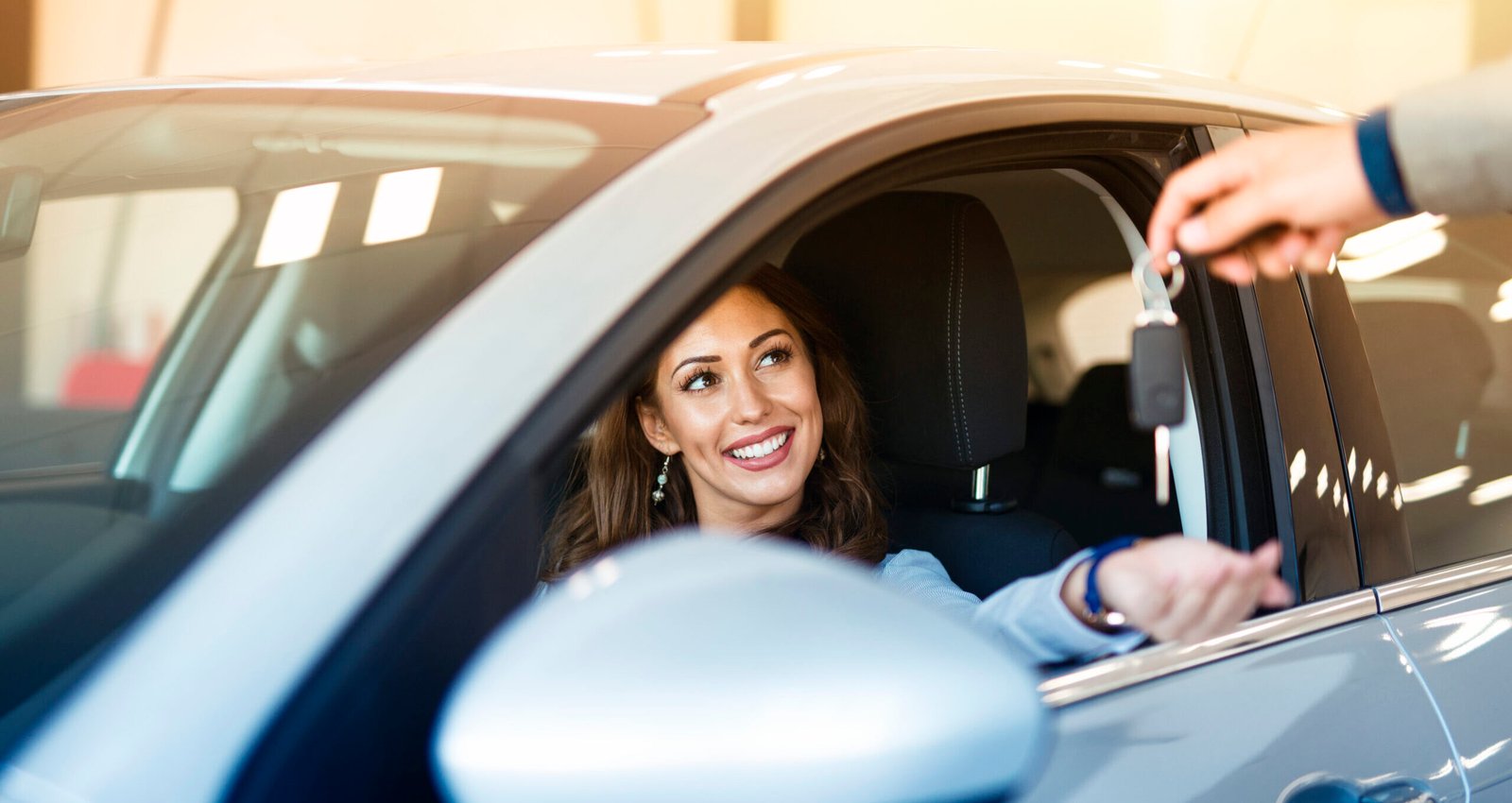 an attractive brunette woman sitting in her brand new car and taking keys from vehicle dealer.